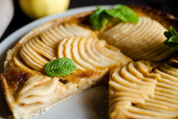 Apple French pie close-up decorated with mint leaves. Open pie with thinly sliced apples in sugar...