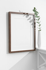 Portrait artwork frame mockup on white wall with eucalyptus twig, blank mock up with copy space