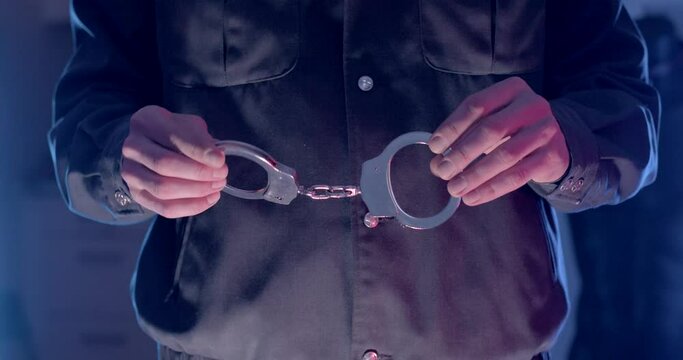 Close-up of a policeman's hand holding handcuffs in his fingers. He's demonstrating a metal handcuffing tool. Offer voluntary surrender, pardon.