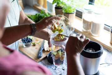 Midsection of biracial senior couple putting fruit slices in mixer while making smoothie in kitchen