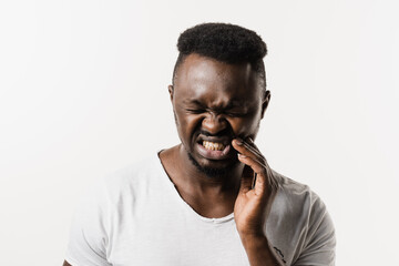 Toothache of african man on white background. African american is touching cheek and feeling teeth hurt on white background. Tooth decay, infection or injury to the tooth or gums.
