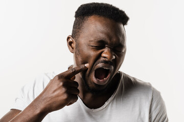 African man with tooth decay, infection or injury to the tooth or gums on white background. African american man is touching cheek and feeling toothache pain and discomfort of tooth.