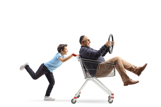 Full length profile shot of a boy pushing a mature man in a shooping cart holding a steering wheel