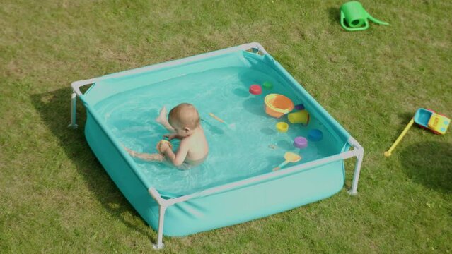 top view baby playing in swimming pool alone, safety concept children in water. toddler child kid sitting in water pool outside house in sunny warm day weather. hot summer activities children outdoors