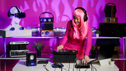 Cheerful performer listening music into headphones while mixing techno sound using professional mixer console. Artist standing at dj table dancing and having fun, enjoying party in night club