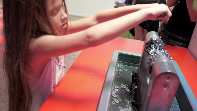 Preschooler girl plays with magnetic device in museum. Kid builds bridge attaching steel washers to big magnets examining magnetic field closeup