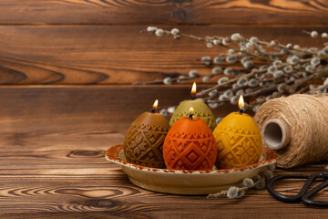 Easter candle eggs in a plate on a brown textural background. Easter holiday concept.Spring willow bouquet.Decor for home and festive steel.Copy space. Place for text.