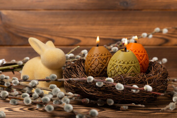 Fototapeta na wymiar Easter candle eggs in a nest with an easter bunny on a brown textural background. Easter holiday concept.Spring willow bouquet.Decor for home and festive steel.Copy space. Place for text.