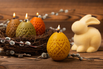 Easter candle eggs in a nest with an easter bunny on a brown textural background. Easter holiday...
