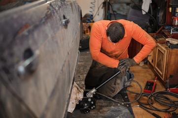 Mechanic man repairs the undercarriage of the car. A man repairs a car in a garage. Car wheel repair