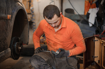 Fototapeta na wymiar Mechanic man repairs the undercarriage of the car. A man repairs a car in a garage. Car wheel repair