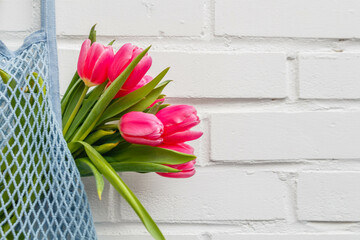 Close-up of pink tulips bouquet in a mesh bag against a white brick wall