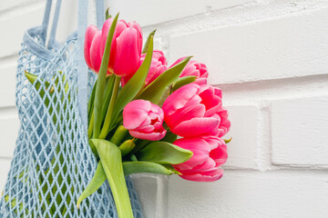 Close-up of pink tulips bouquet in a mesh bag against a white brick wall