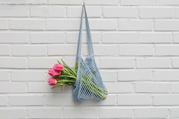 Pink tulips in a mesh bag against a white brick wall