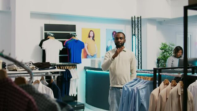 African american shopper using hologram in boutique to check new clothing store merchandise with augmented reality. Male customer looking at holographic footage, artificial intelligence.