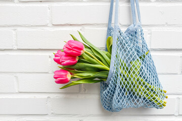 Pink tulips bouquet in a mesh bag against a white brick wall