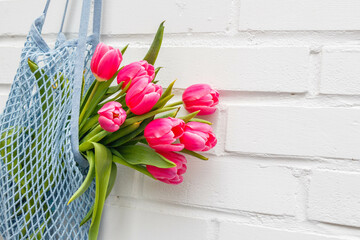 Close-up of pink tulips bouquet in a mesh bag against a white brick wall