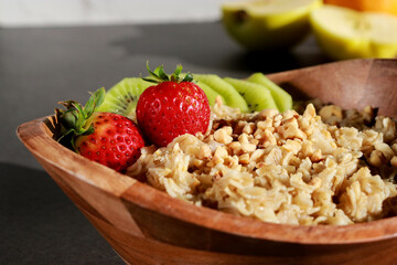close up of healthy homemade oatmeal in a wooden bowl with fruits on table