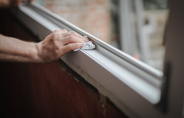 Hands of a Caucasian man cleans the window frame.