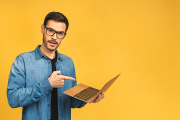 Confident business expert. Confident young handsome bearded man in casual holding laptop and smiling while standing over isolated yellow background. - 580872169