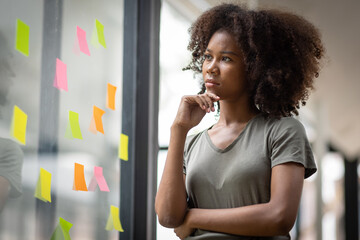 A black American african business woman in afro hairstyle planning in meeting at office and use post it notes to share idea. Brainstorming concept. Sticky note on glass wall.