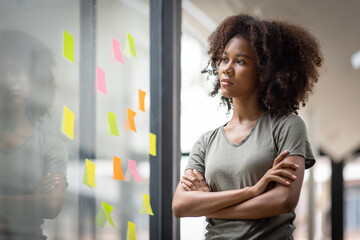A black American african business woman in afro hairstyle planning in meeting at office and use post it notes to share idea. Brainstorming concept. Sticky note on glass wall.