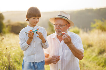 Fototapeta premium Little boy with his grandfather standing in a field with two toys plane at summer