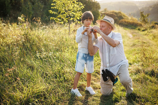 Little boy with his grandfather standing in a field with a binoculars at summer