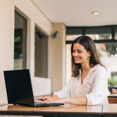 Vertical portrait of a beautiful Caucasian female student is studying at university by distance learning. She is sitting at a table at home with a laptop and a notepad