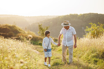 Fototapeta na wymiar Photo of a little boy with his grandfather walking in a field at summer
