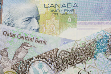 A colorful blue five dollar bill from Canada with colorful riyal notes from Qatar