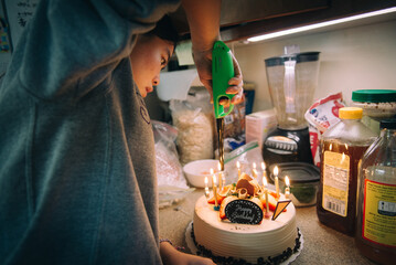 Young asian girl lighting birthday candles in dark kitchen