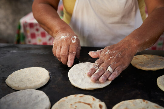 Woman flipping a corn tortilla with a spatula in a hot griddle