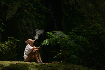 Young woman smokes a vape in the jungle on a tropical island, Bali.