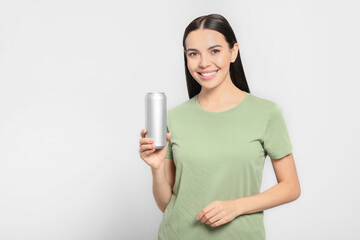 Beautiful happy woman holding beverage can on light grey background. Space for text