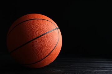 Obraz premium Basketball ball on black wooden table against dark background, space for text