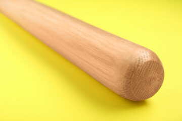 Wooden baseball bat on yellow background, closeup. Sports equipment