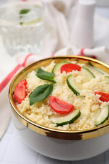 Tasty couscous with tomatoes, cucumber and basil on white tiled table, closeup