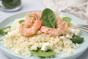 Delicious couscous with shrimps and spinach served on white table, closeup