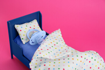 Fototapeta na wymiar Maternity leave concept. Toy bed with baby pacifier on pink background