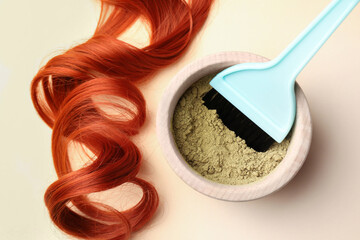Bowl of henna powder, brush and red strand on beige background, flat lay. Natural hair coloring