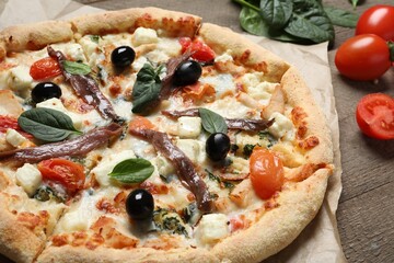 Tasty pizza with anchovies and ingredients on wooden table, closeup