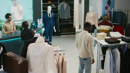 Multiethnic group of people looking at trendy clothes in retail store market, shopping for formal or casual wear. Diverse customers examining fashion collections on hangers, commercial activity.