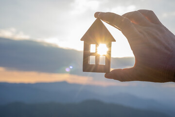 hand holds wooden house against the sun. estate sold agent concept