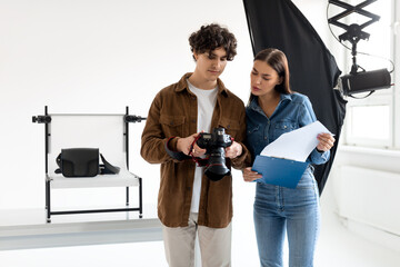 Young female assistant of professional photographer with documents discussing details of photo...