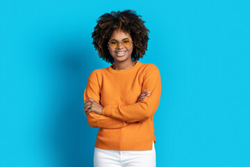 Positive black woman posing with arms crossed over blue background