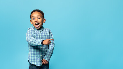 Special offer. Adorable african american boy pointing finger aside at copy space and looking at camera with open mouth - obrazy, fototapety, plakaty