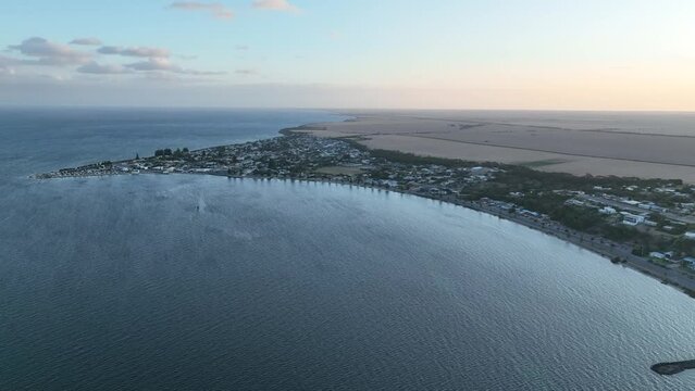 Drone shot of Port Vincent beach town. Camera high above the ocean, entire town visible shot. Farm land also visible.  Shot at sunset. South Australia Tourism