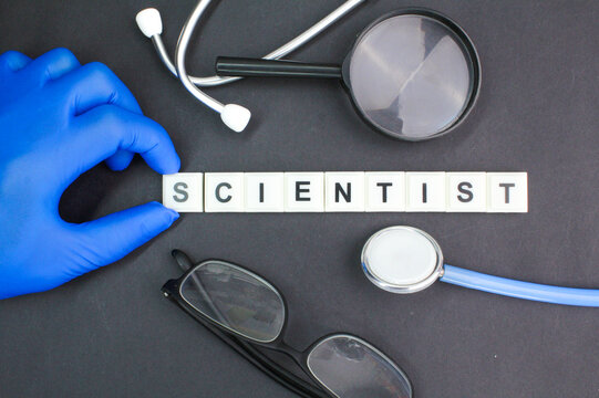 stethoscope, magnifying glass and glasses with hands holding the word scientists. research concept