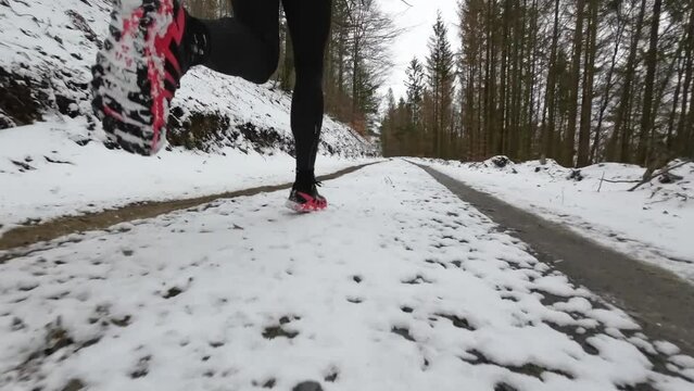 Close up rear view of a trail runner pacing on wintery forest trails. Shoes are red and the runner applies a forefoot or midfoot strike.